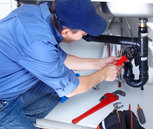 A uniformed Hydrofix Plumbing technician uses a wrench to repair a leaking kitchen sink P-trap in Auckland